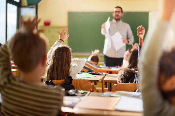 istock Back view of students raising their hands to answer the teacher's question on a class. 2204837959