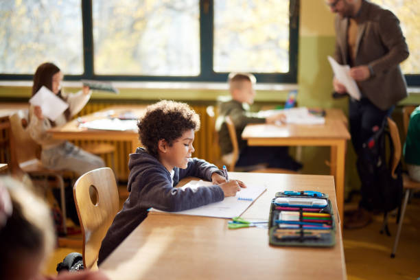 istock Happy black schoolboy writing on a class at elementary school. 2204838042