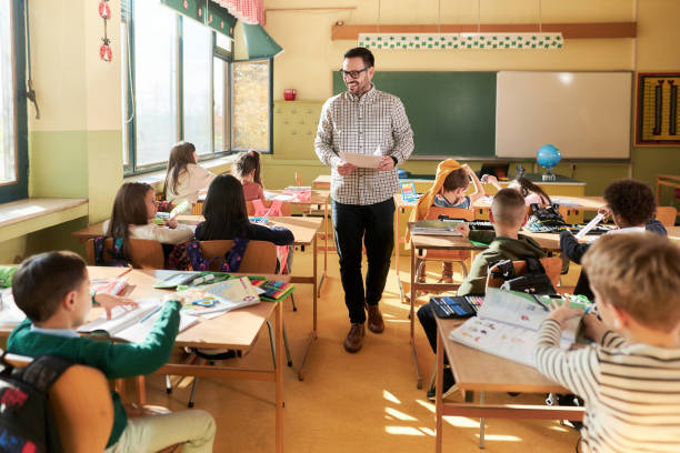 istock Young happy teacher talking to elementary students on a class in the classroom. 2204838111