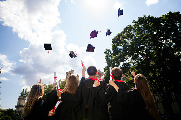 Rear portrait of group students hands throw mortarboard graduation university building outdoors.