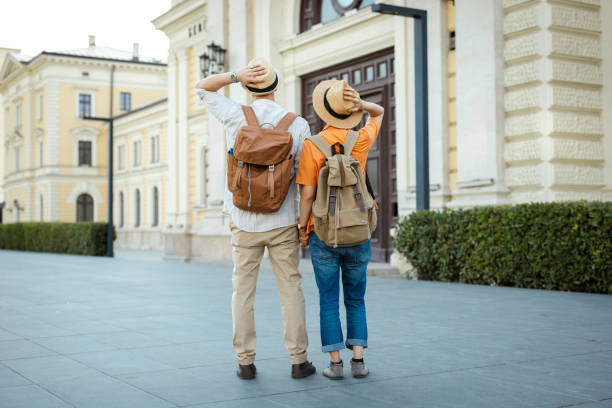 Two individuals wearing hats and backpacks admire the architecture of a historic city street.