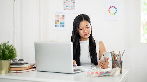 istock An asian woman is holding a stylus drawing or writing on a graphic tablet while looking at phone. 2204848593