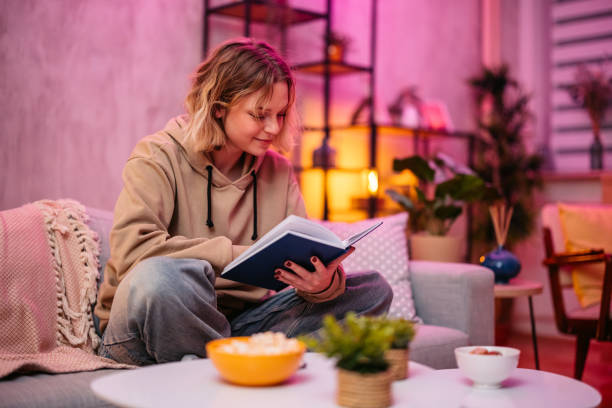 istock Young Woman Reading A Book While Sitting On The Sofa At Home At Night 2204848808
