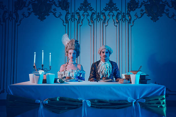 istock Two people dressed in period costumes sit at a dinner table in a modern setting with bright neon lighting. 2204848964