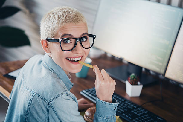 istock Cheerful female programmer at her desk enjoying a snack while working in a bright office space 2204850042