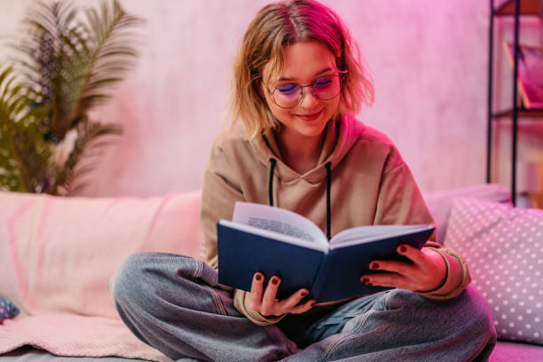 istock Young Woman Reading A Book While Sitting On The Sofa At Home At Night 2204850286
