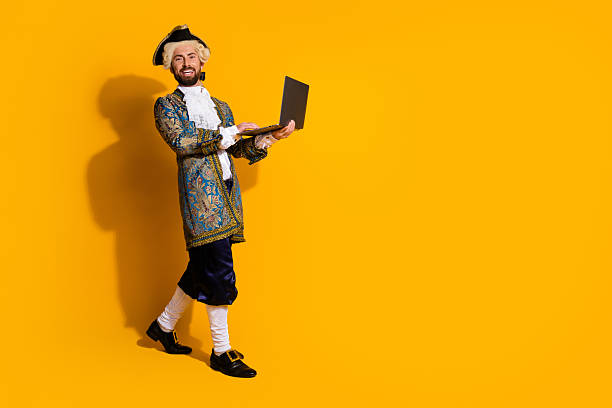 istock Modern comparison: young man in noble costume using a laptop on yellow background 2204851613