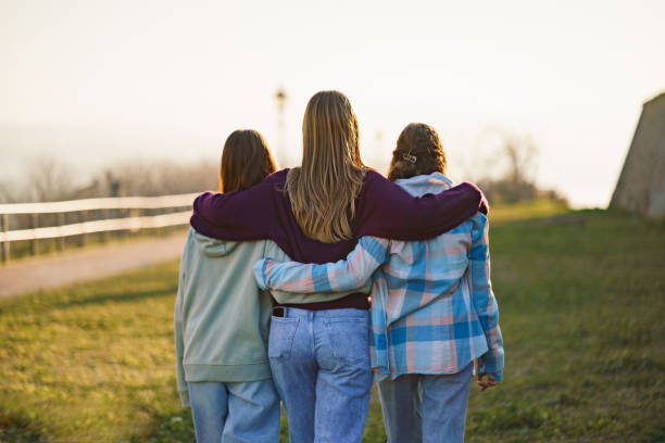 Rear view of teenage girls embracing during sunny day outdoors