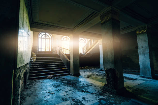 istock Abandoned grand building, large staircase to darkness, sunlight through arched windows, decayed walls, debris 2204852499