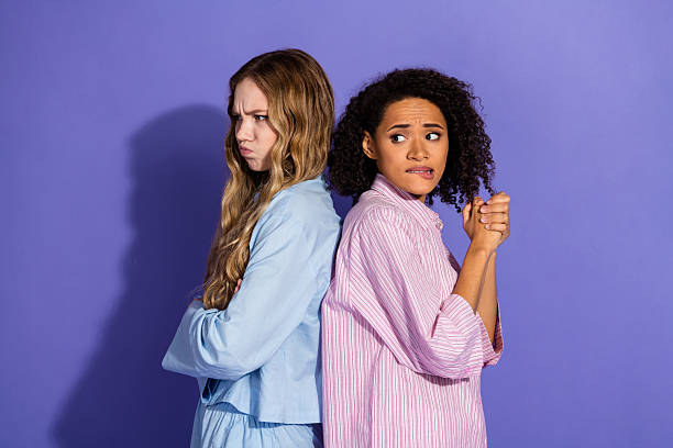 istock Two young women standing back to back expressing contrasting emotions on a purple background, wearing trendy nightwear 2204853673