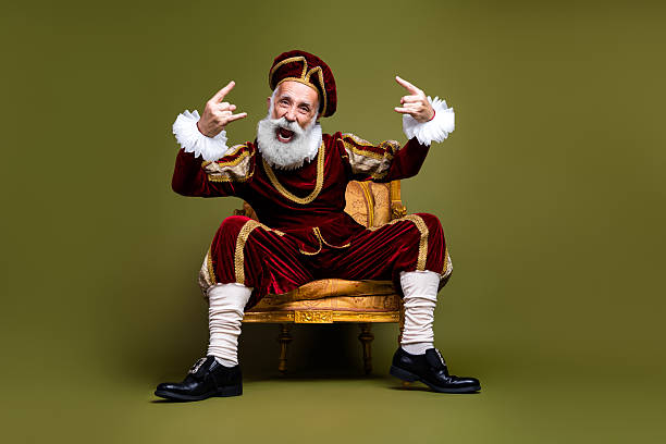 istock Vintage styled elderly man in royal attire with playful gesture on a khaki backdrop 2204854548