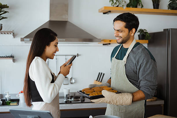 istock Woman Capturing Fresh Bakes as Man Presents Muffin Tray 2204855130