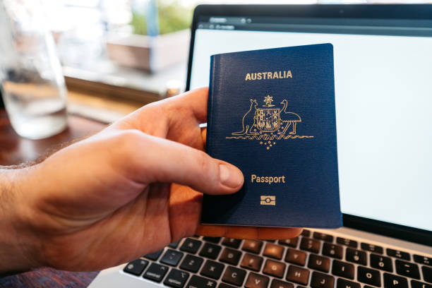 istock Mid-Adult Man Holding An Australian Passport While Using Laptop At Home 2204855805