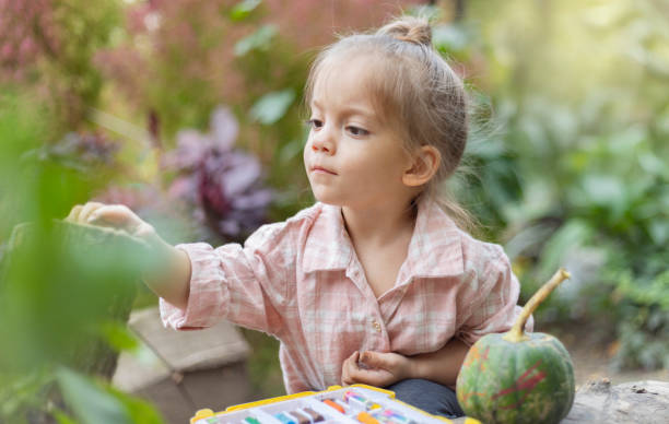 istock A young child paints a small pumpkin outside, surrounded by nature. This image captures the simplicity and joy of seasonal creativity. 2204858348
