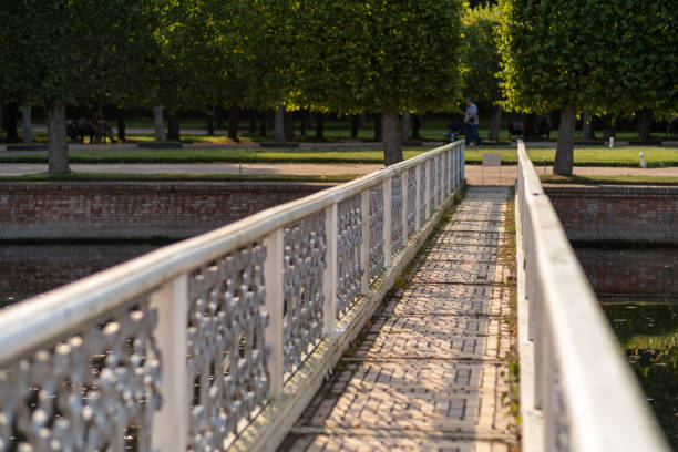 Visitors enjoy a leisurely stroll on the bridge at Peterhof gardens surrounded by lush greenery and serene water features under a clear sky