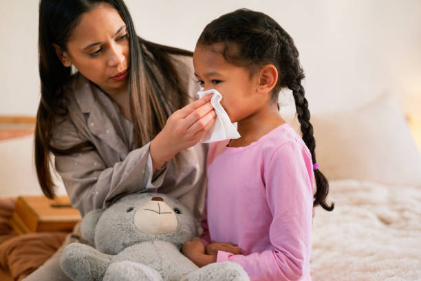 istock Sick, help and mother with kid for blowing nose on bed with cold, flu or allergies symptoms. Care, tissue and mom with girl child for sinusitis with hayfever illness in bedroom together in home. 2204861915