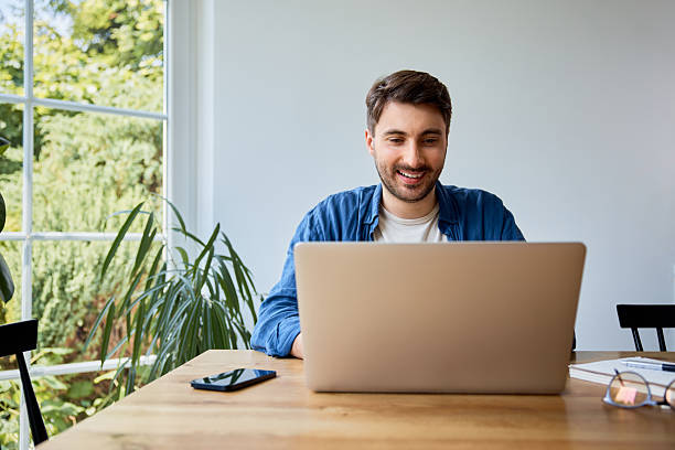 istock Happy young man working on laptop at home sitting at table 2204868219