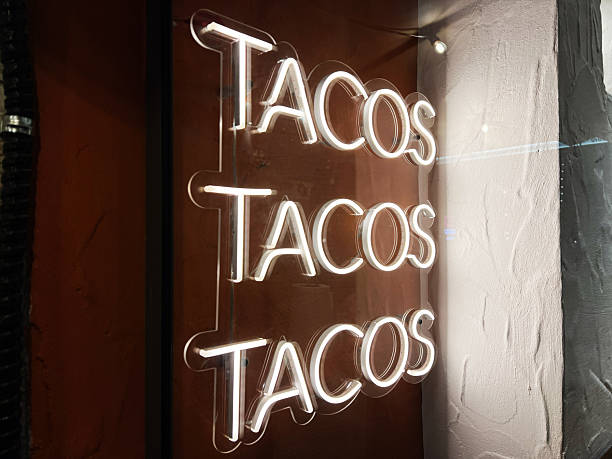 Illuminated neon tacos sign with a vibrant design on a textured wall