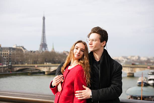 A smiling couple embraces on a scenic Parisian bridge, overlooking the Seine River with the Eiffel Tower behind them. Loving pose capture a timeless romantic moment in the heart of France.
