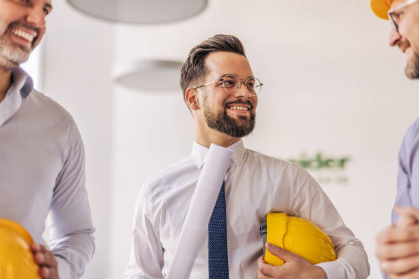 istock Smiling architect holding blueprints and discussing project with colleagues 2204871431
