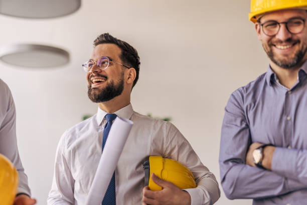 istock Architects smiling and holding blueprints and yellow hardhats 2204871482