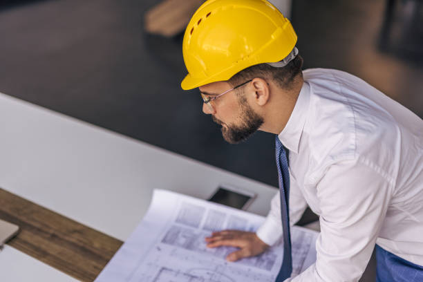 istock Architect wearing hardhat studying blueprint in the office 2204872442