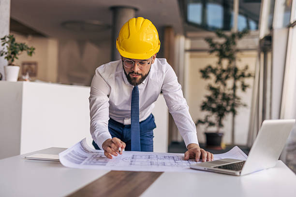 istock Architect wearing hardhat studying blueprint in office 2204872458