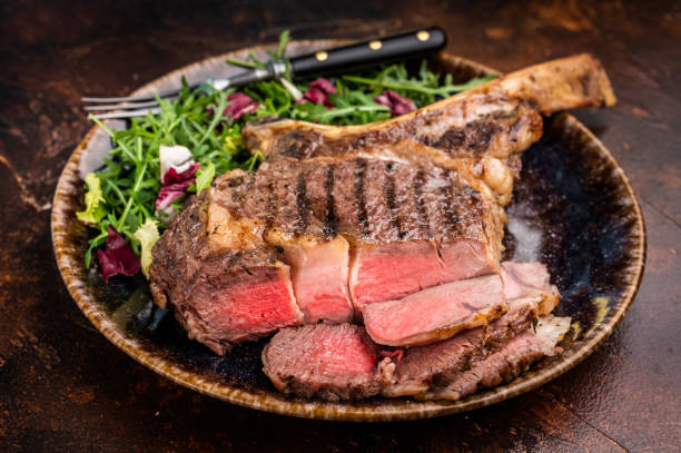 istock Grilled and sliced Tomahawk beef steak, marble  rib eye with bone on plate with salad. brown background. top view 2204874052
