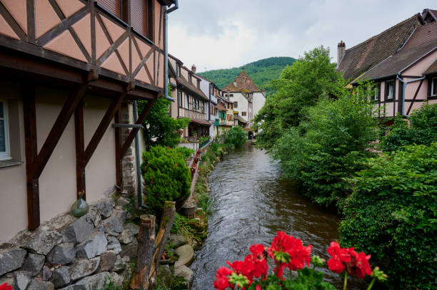 A peaceful river winds through Kaysersberg with lush greenery and quaint homes.