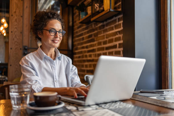 istock Freelancer working on laptop in coffee shop smiling and looking away 2204876351