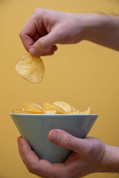 istock hand getting some potato chips out of a bowl. yellow background. 2204876828