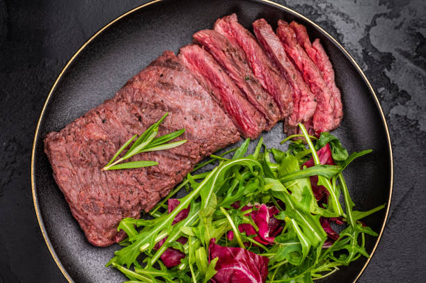 istock Grilled and sliced Flank beef steak on plate with salad. black background. top view 2204879136