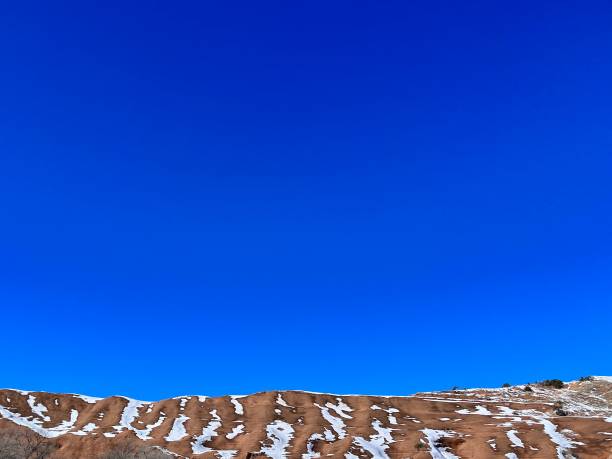 Red rocks and snow patches create a striking contrast against a vibrant, deep blue sky in Gallup, New Mexico, offering a serene and picturesque winter landscape along the historic Route 66