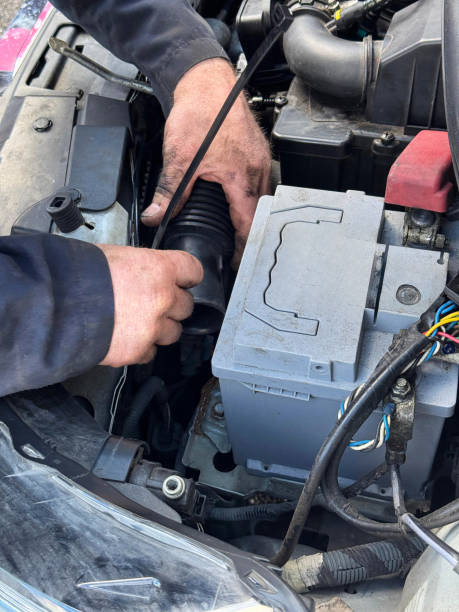 istock Full frame image of unrecognisable car mechanic wearing blue overalls working on car engine, oily hands, open car bonnet displaying engine, air intake pipe being tightened with plastic cable tie by vehicle mechanic, elevated view focus on foreground 2204882221