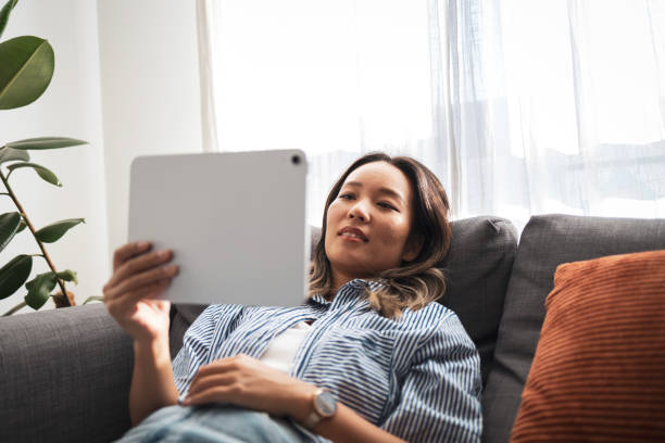 istock Asian woman relaxing on a sofa using a digital tablet 2204888660