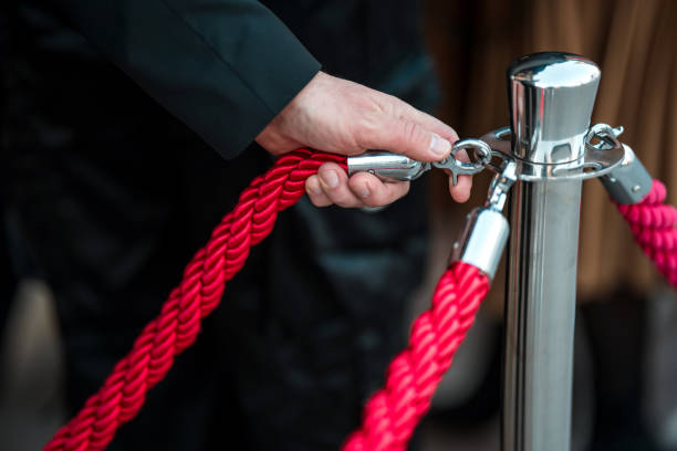 istock Close-Up on Security Personnel's Hand Securing Red Rope Barrier with Metallic Post 2204891972