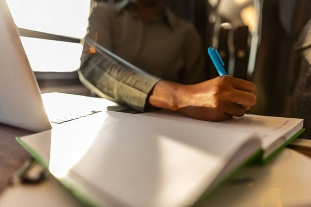 istock Person Writing Notes by Laptop in Sunlit Workspace 2204892594