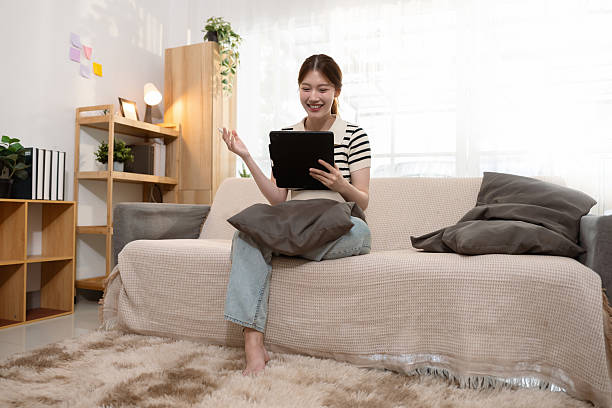 istock Happy woman having fun doing video call using mobile phone sitting on sofa. 2204896874