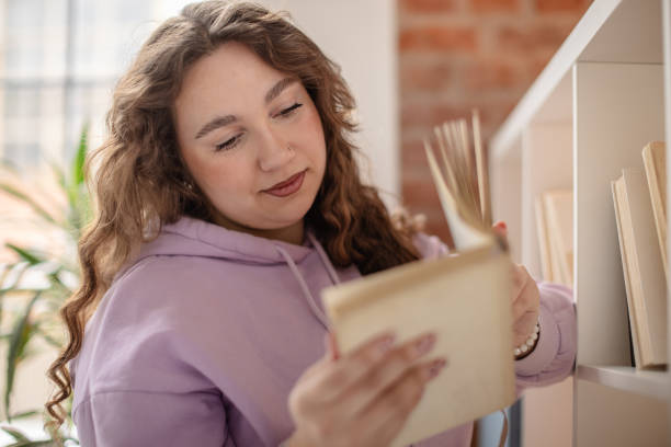 istock Plus size young woman enjoying her time at home while browsing through books in a cozy living room 2204897448