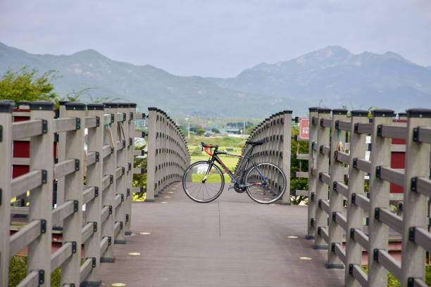 Gokseong County, South Korea - October 3rd, 2021: A road bike rests on a wooden bridge along the Seomjin River cycling path, with a backdrop of lush fields and towering mountains.