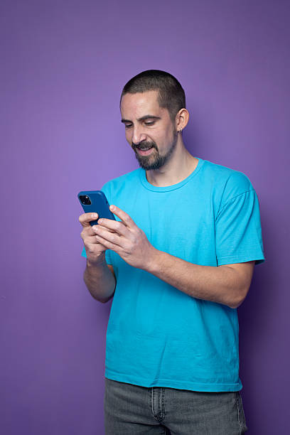 istock Man is actively engaged with his smartphone, set against a vibrant purple background 2204901924
