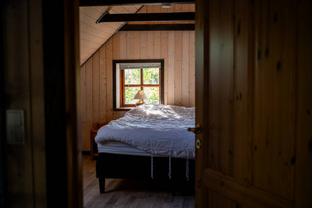 Warm rustic bedroom with wooden walls, bed with white linens and sunlight streaming through a window, creating a peaceful and cozy atmosphere