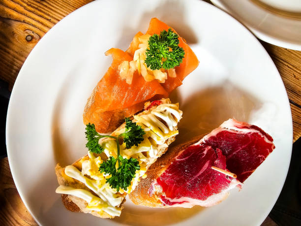Overhead view of three different tapas pieces of food on the plate at a restaurant. One has fresh Iberico ham, the other smoked salmon.