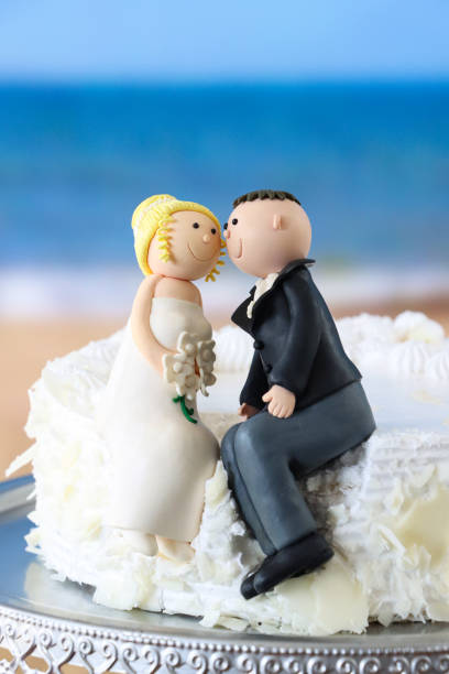 istock Image of couple on beach under blue sky, white wedding cake and fondant icing bride, bridgegroom toppers / cake figurine, sweet food 2204909056