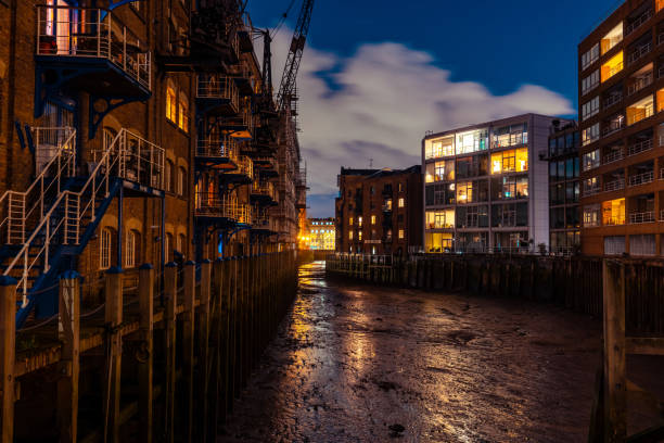 Low tide reveals the muddy riverbed between illuminated buildings in london's docklands at night
