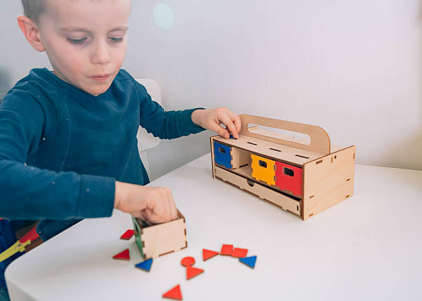 istock A little pupil arranges multicolored geometric shapes in a chest with multicolored boxes: red, yellow, green and blue. geometric shapes of different colors are scattered on the table. This Montessori-inspired developmental exercise develops coordination 2204911347