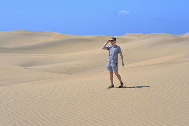 istock A young man walking along a sand dune through barkhan in Maspalomas, Gran Canaria on a hot sunny day. Desert travel touristic concept 2204911666