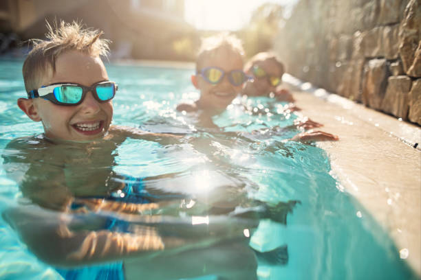 istock Three kids playing happily in swimming pool 2204911897