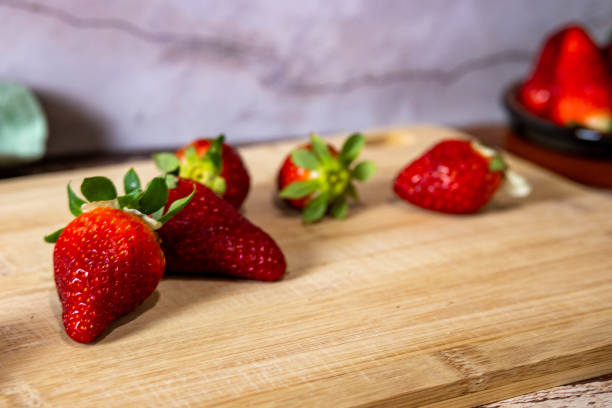 A wooden cutting board with five strawberries on it