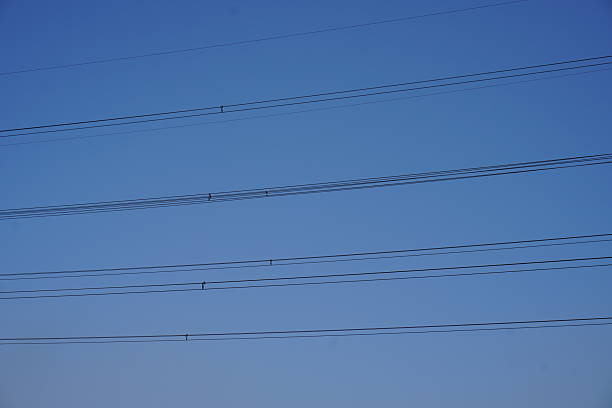 The overhead high-voltage electric wires are going towards the locality for power supply against the clear blue sky background